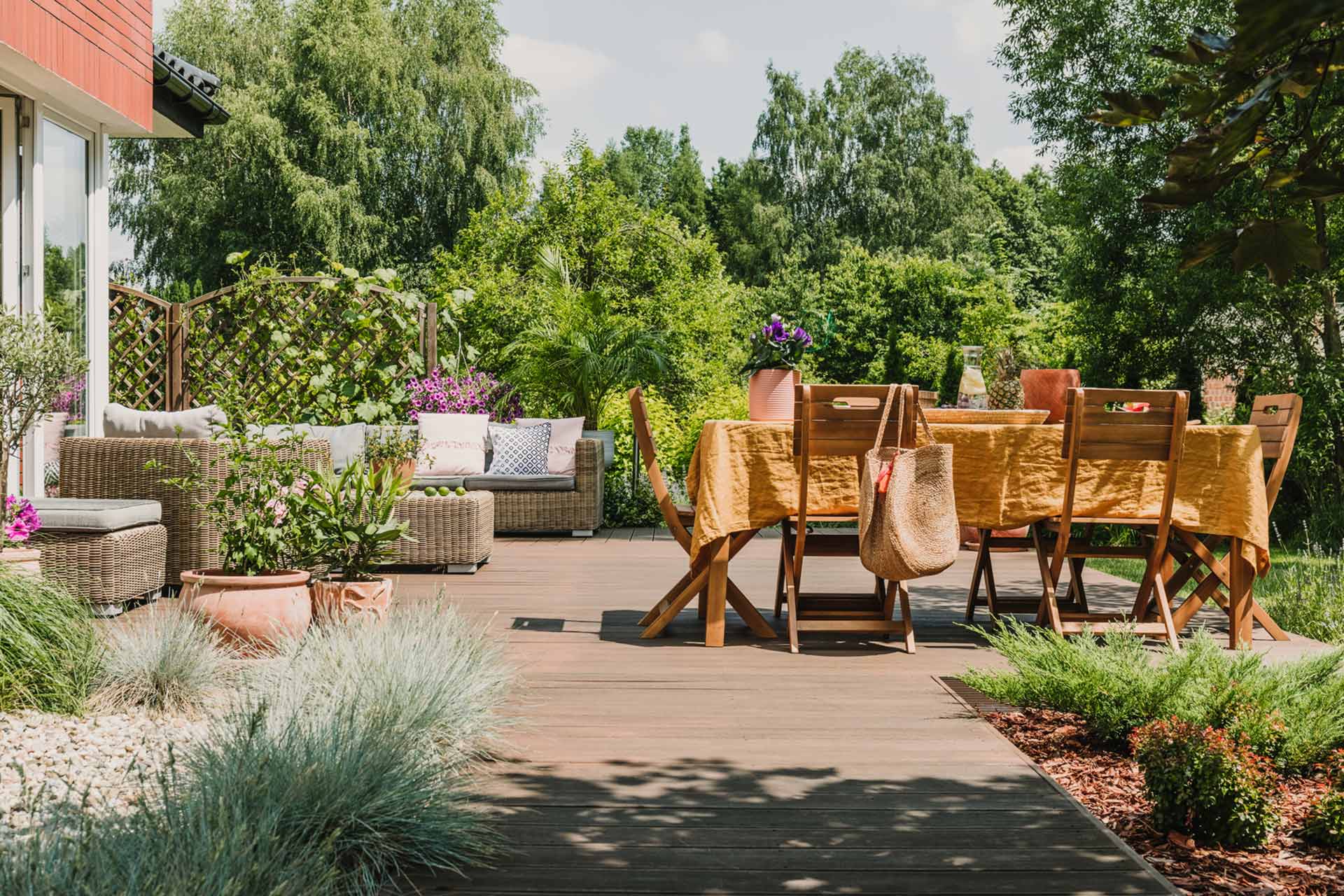 Gartenterrasse mit Holzboden, Esstisch und Gartenmöbeln in natürlicher Umgebung